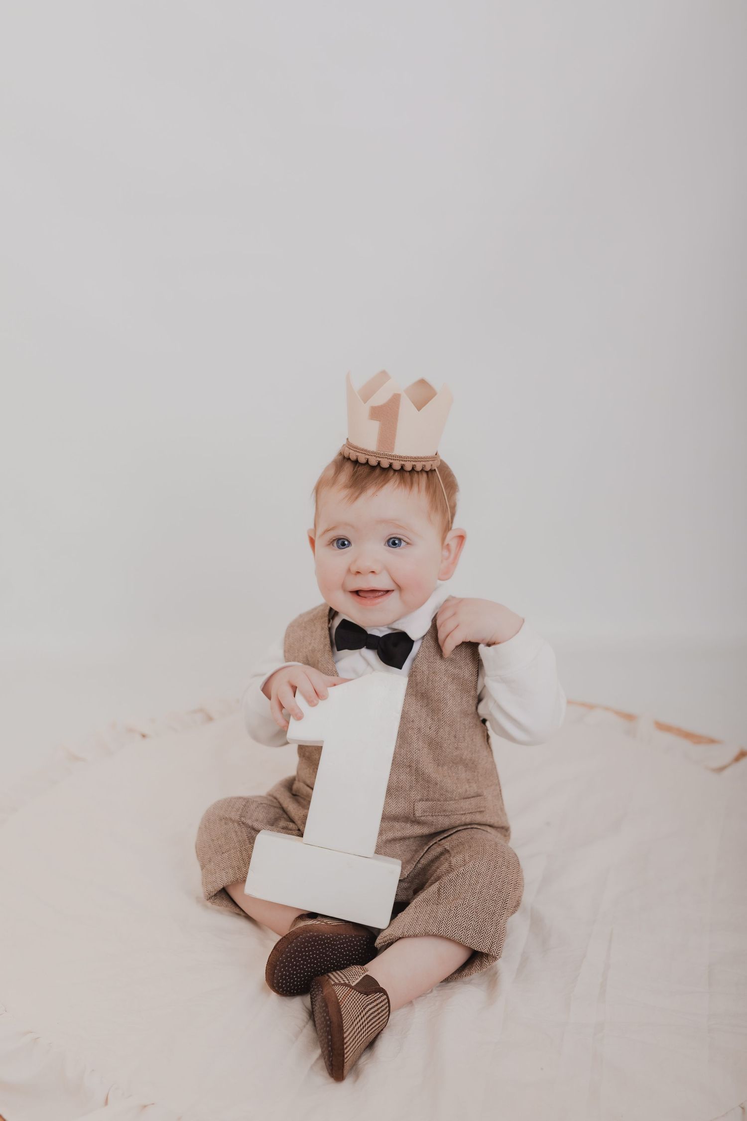 Baby in brown formal outfit with bow tie holding number one prop against white background. Photographer. Hull. East Yorkshire. Photography