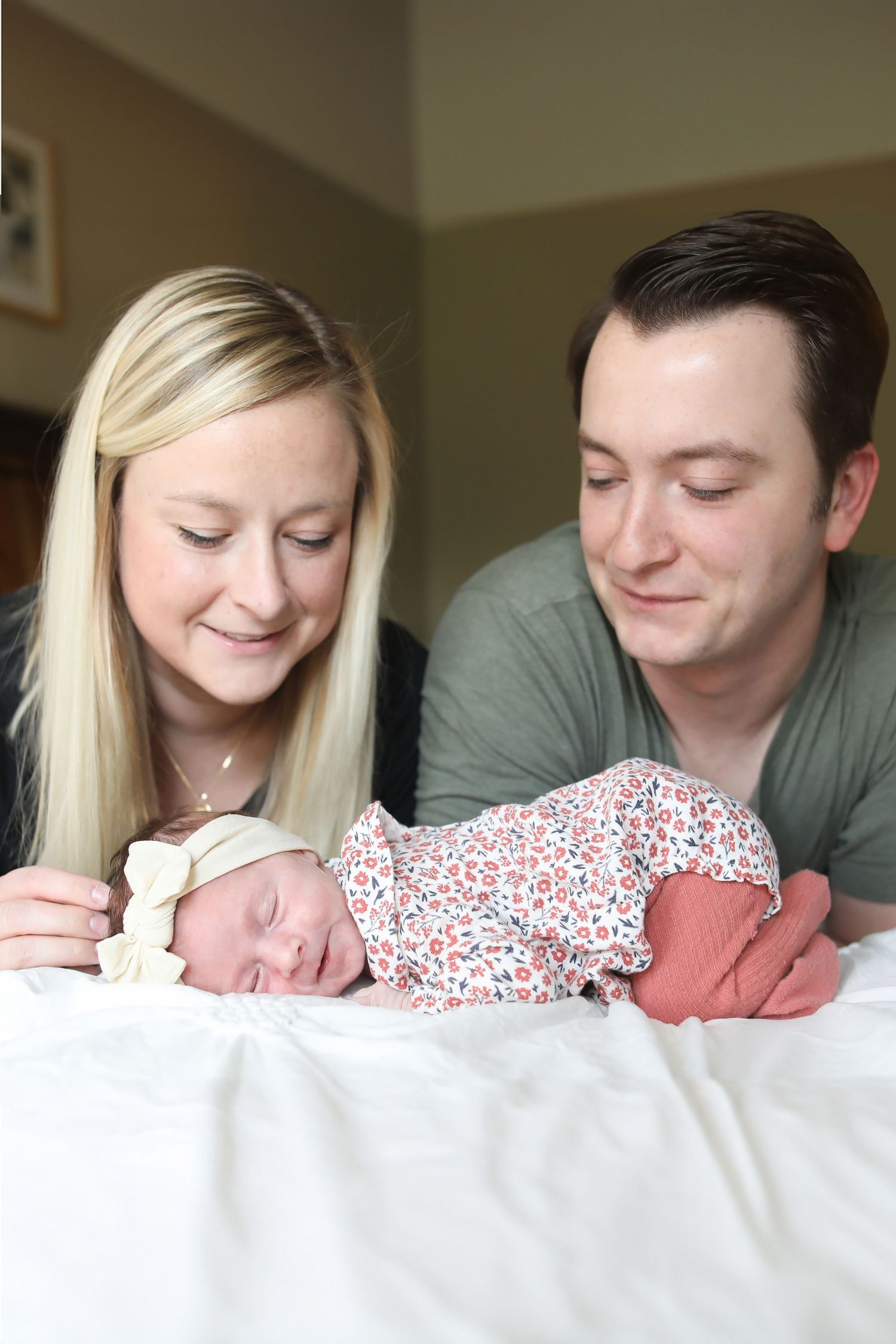 Parents lovingly gazing at newborn baby wearing floral outfit on white bedding.