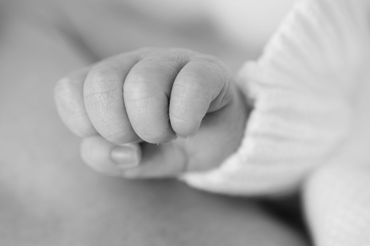 Close-up black and white photograph of tiny baby fingers grasping fabric.