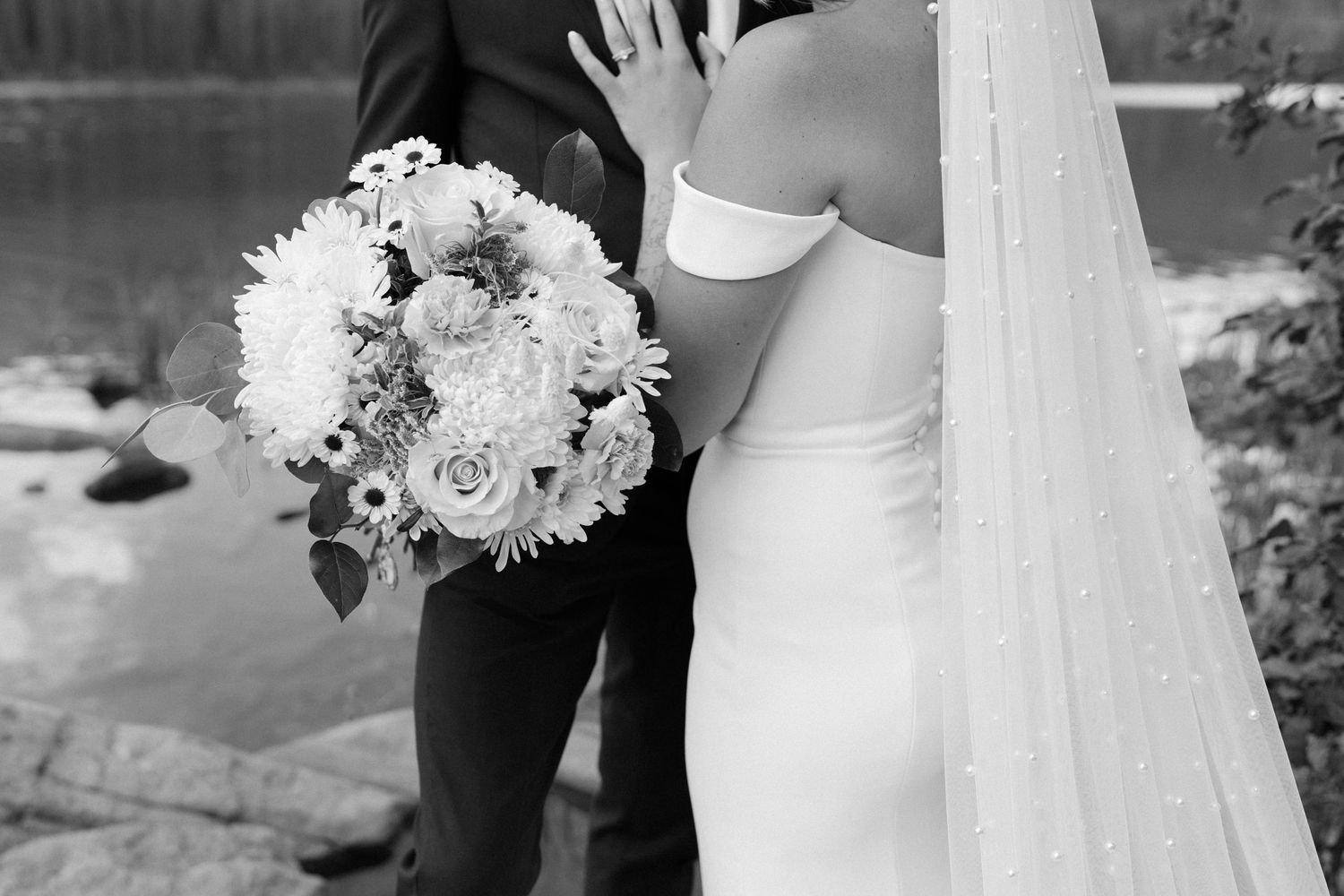 Close-up details of a white wedding dress and bouquet against dark formal attire.