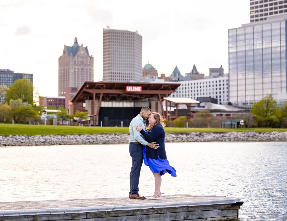 A couple embraces on a wooden dock overlooking the Milwaukee skyline and Lake Michigan on a spring day.