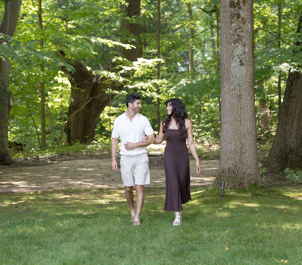 Two people in casual attire take a peaceful stroll along a shaded forest path on a sunny summer day.