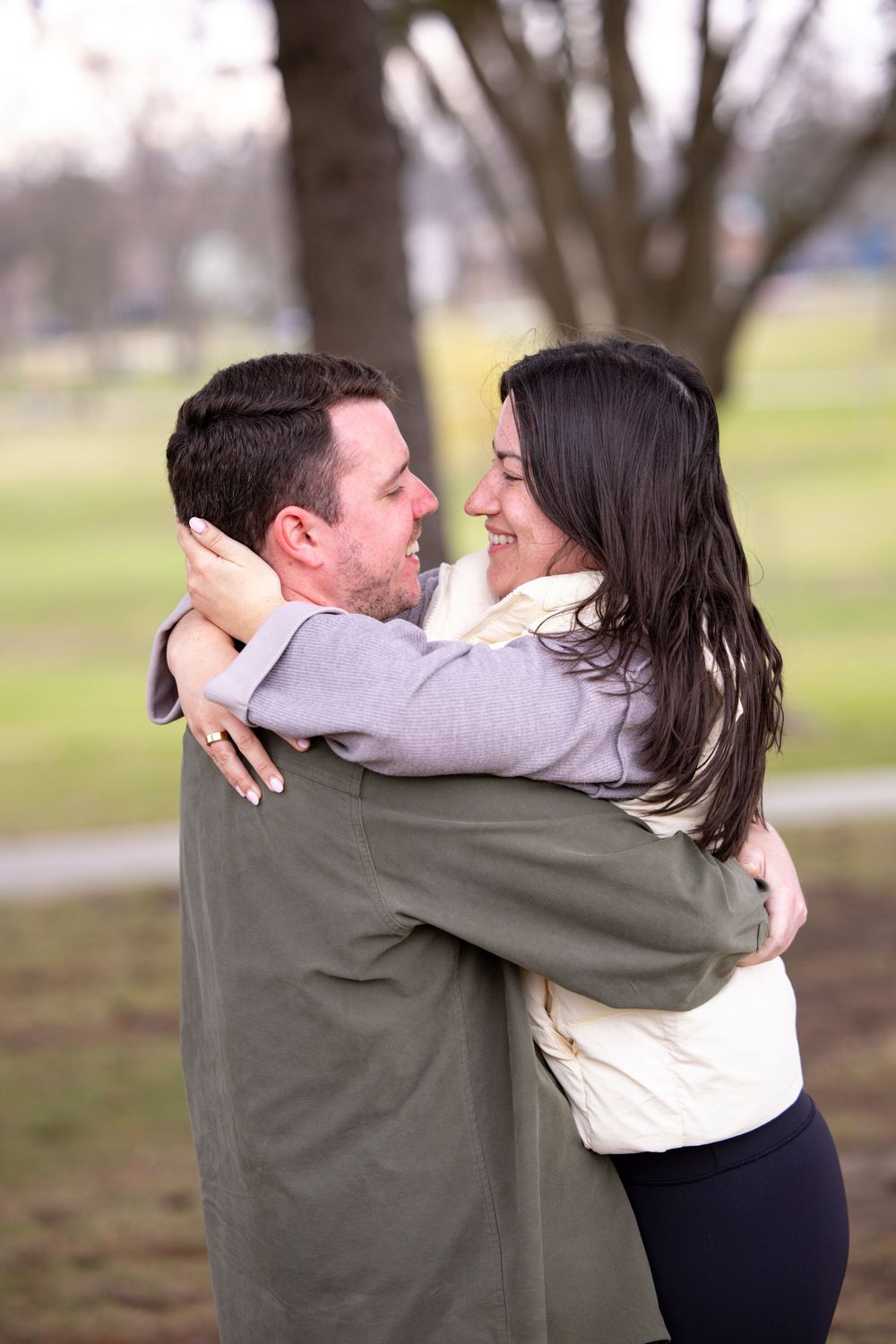 A couple embraces outdoors in a park on an overcast day, sharing a tender moment together.