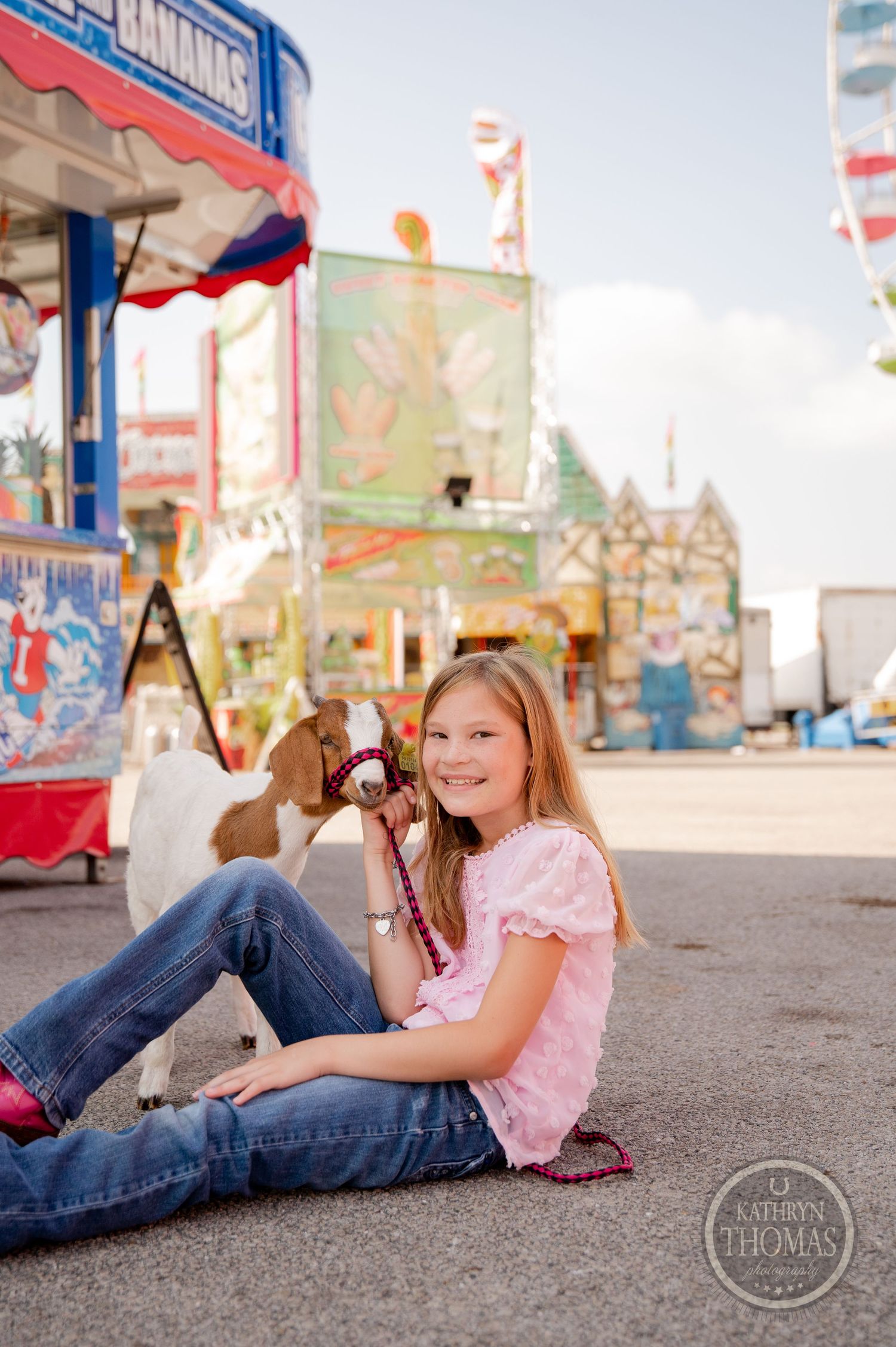 A person sits casually on carnival grounds with game booths and rides visible in background.