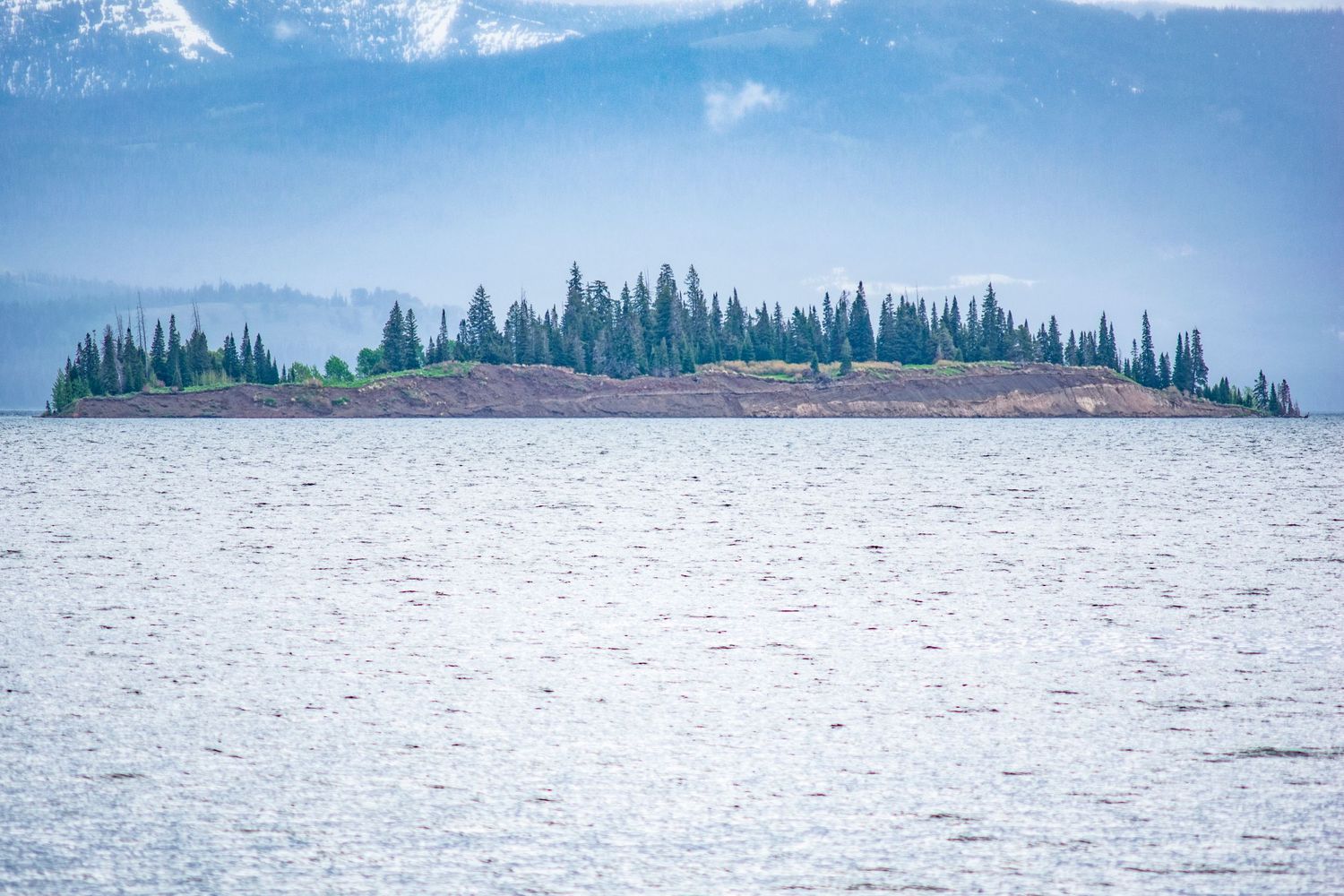 Small forested island on a misty lake with pine trees lining the ridge.