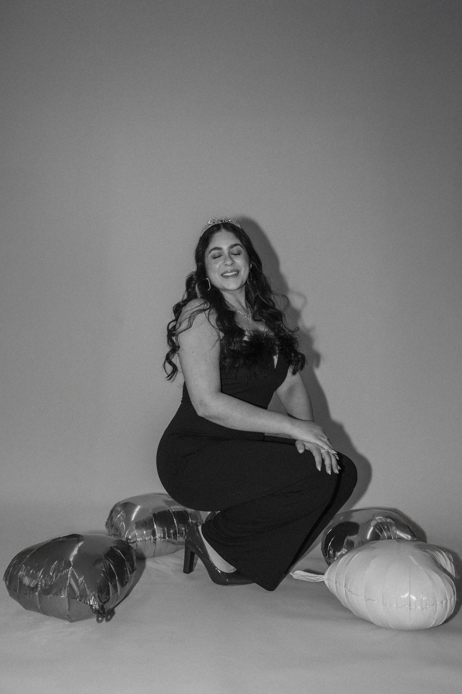 Woman in black dress posing with silver balloons on studio floor.