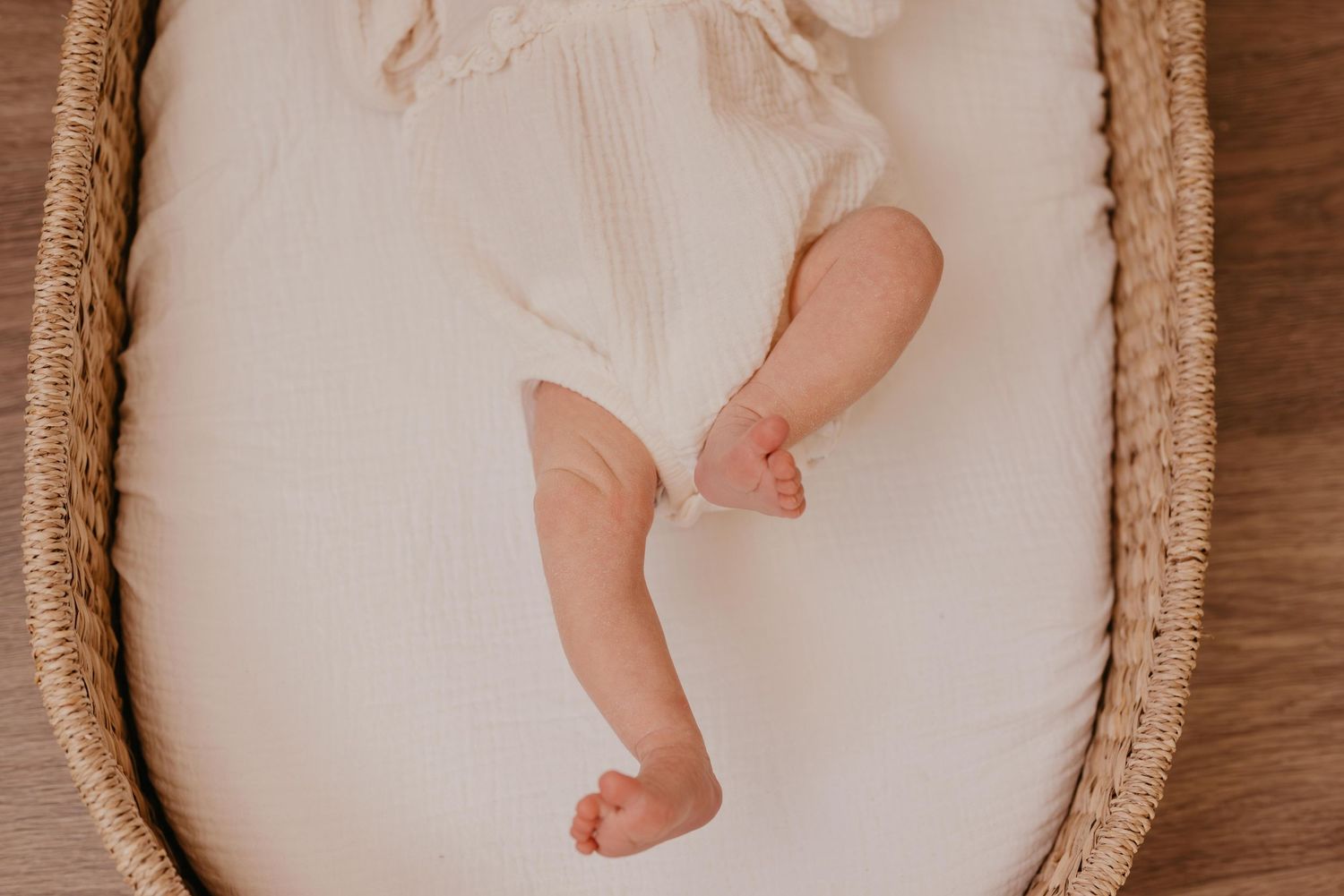 Sleeping newborn baby wearing a pink bow headband swaddled in neutral colors.