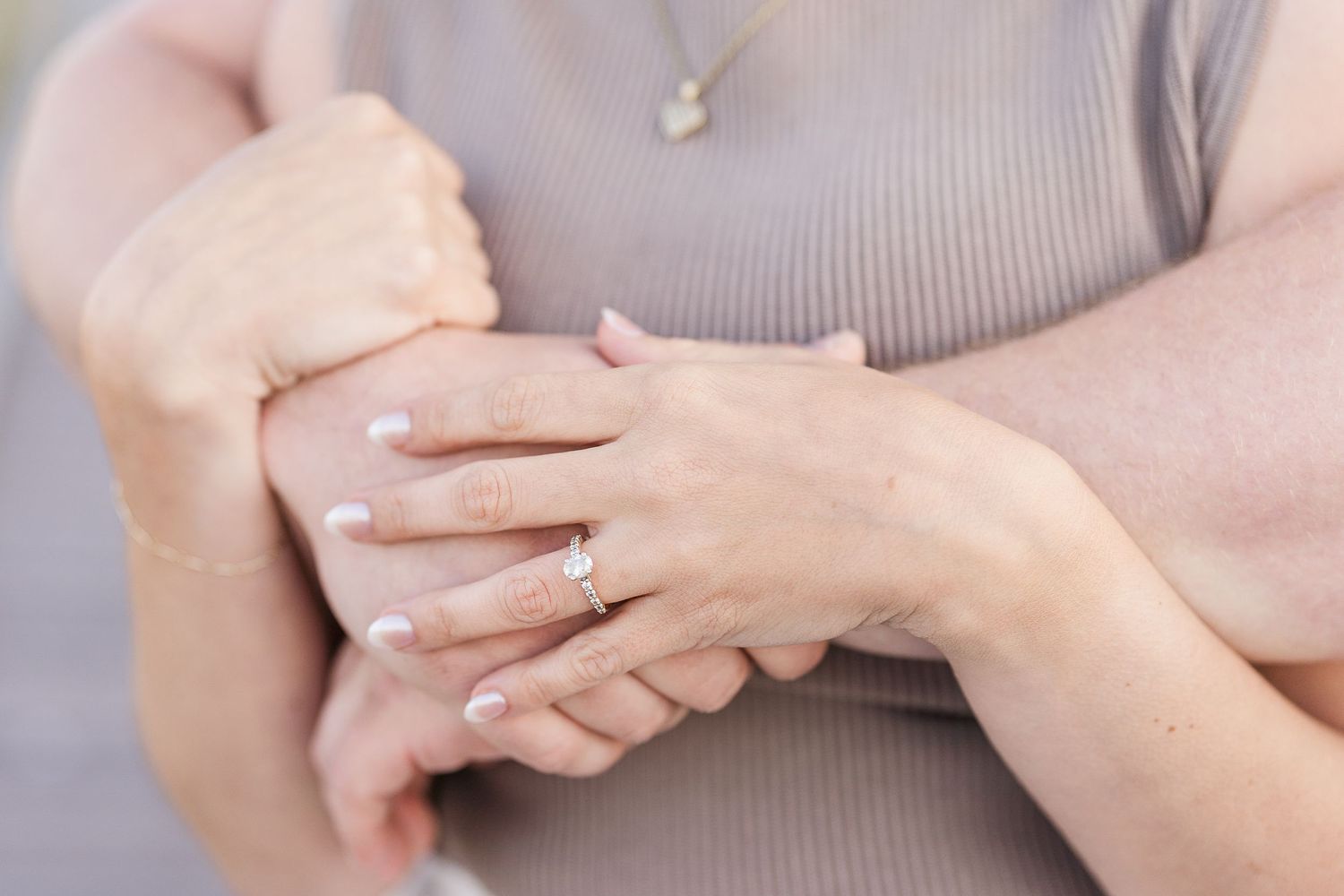 Close-up of a woman's hands folded together wearing a delicate diamond engagement ring.
