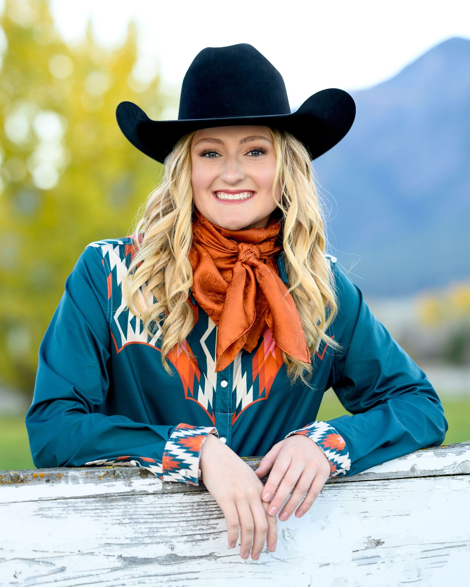 Western style portrait with black cowboy hat and orange scarf against mountain backdrop.