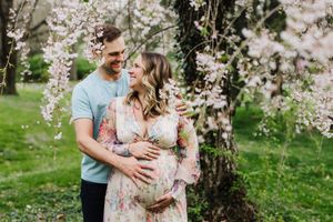 A couple shares a tender moment under blooming cherry blossom trees in a spring garden setting.