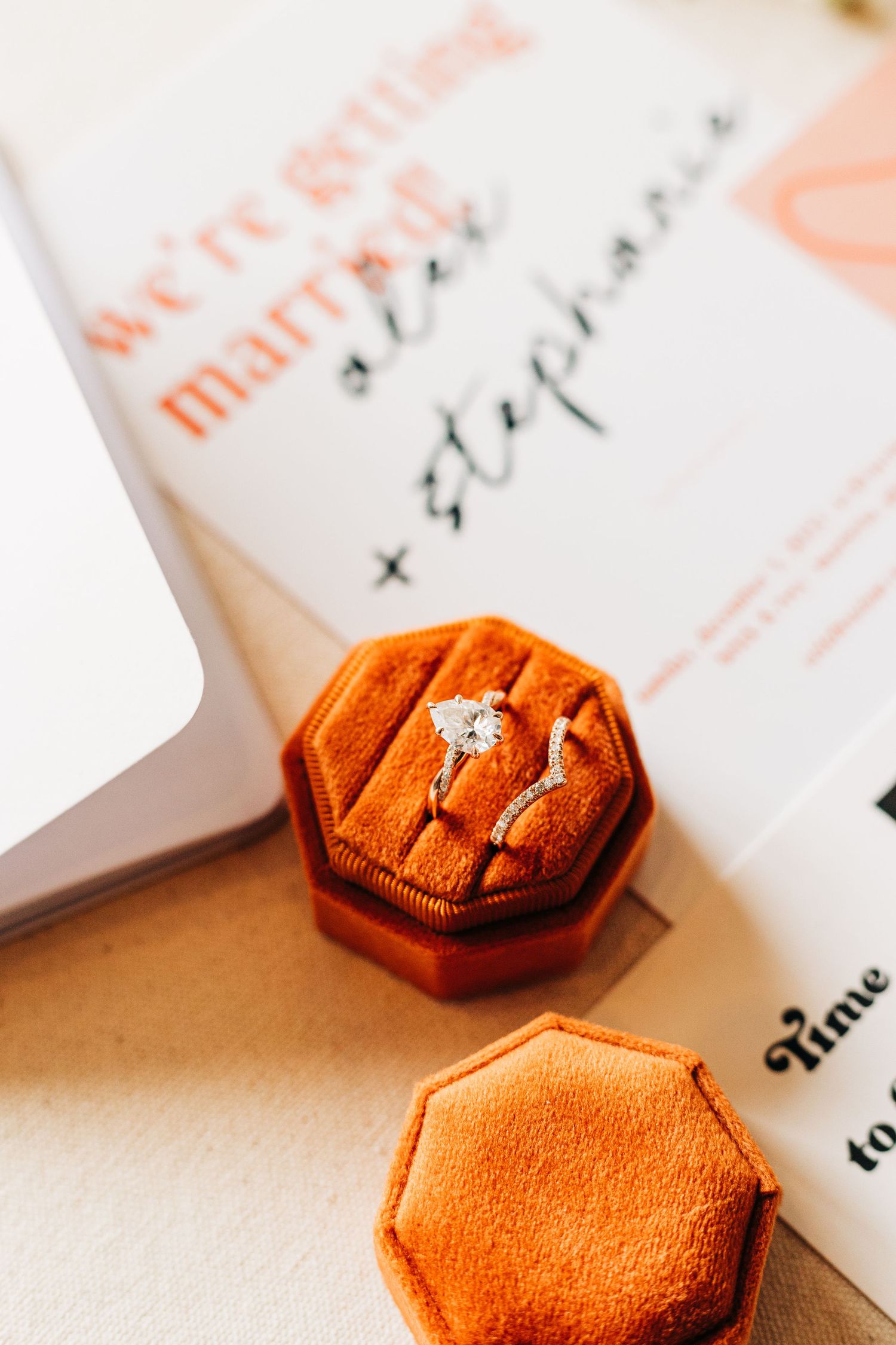 Close-up of engagement ring in orange velvet ring box on wedding invitation.