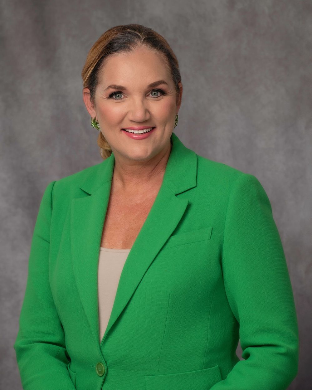 Professional woman in bright green blazer smiling confidently against a gray studio background.