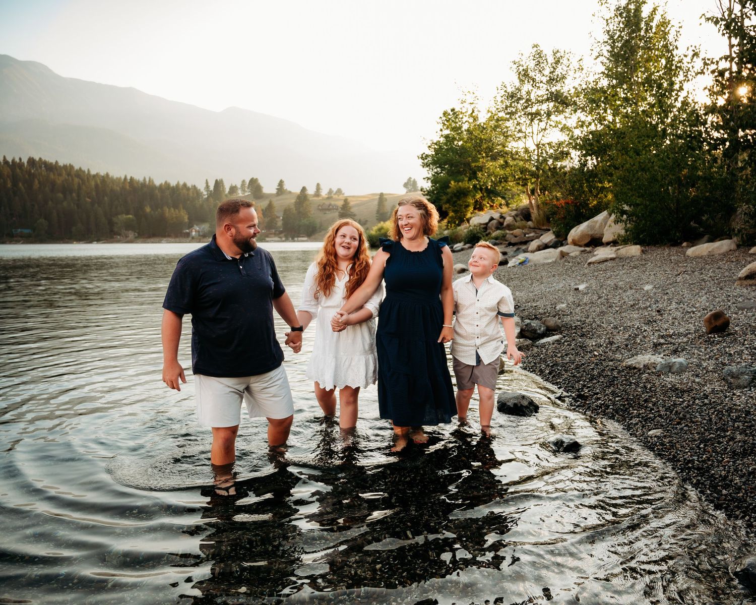 Group walking in shallow water along a rocky lake shore with mountains in the distance.  Wallowa Lake, Joseph, Oregon
