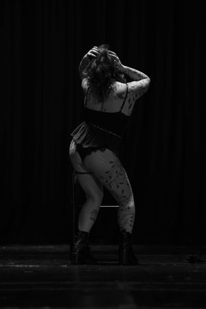 Dramatic black and white stage photo of a performer in edgy attire striking an expressive dance pose against dark backdrop.