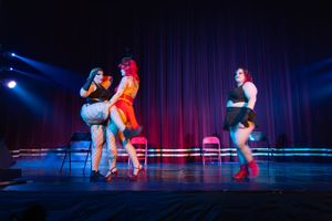 Performers on stage with blue lighting dance during a theatrical show in front of red curtains.