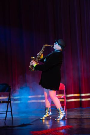 Saxophone player in dramatic lighting performs on stage with colored blue and red lighting effects and black curtains.