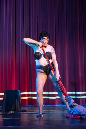 Dramatic burlesque dancer performs a flexible dance routine on stage with purple and red theatrical lighting.