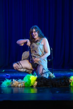 A performer in colorful stage lighting lies on the ground during an artistic theatrical performance.