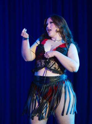 Stage performer in fringe skirt and lace top dances energetically under blue stage lights.