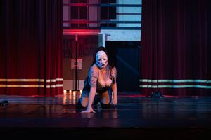 A performer in a red and blue lit stage crouches in a dramatic pose during a theatrical production.