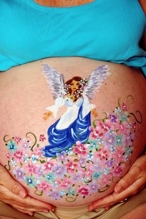 Whimsical angel figure painted on pregnant belly surrounded by pink flowers.