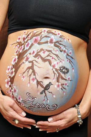Cherry blossom tree painted on pregnant belly with small bird perched on branch.
