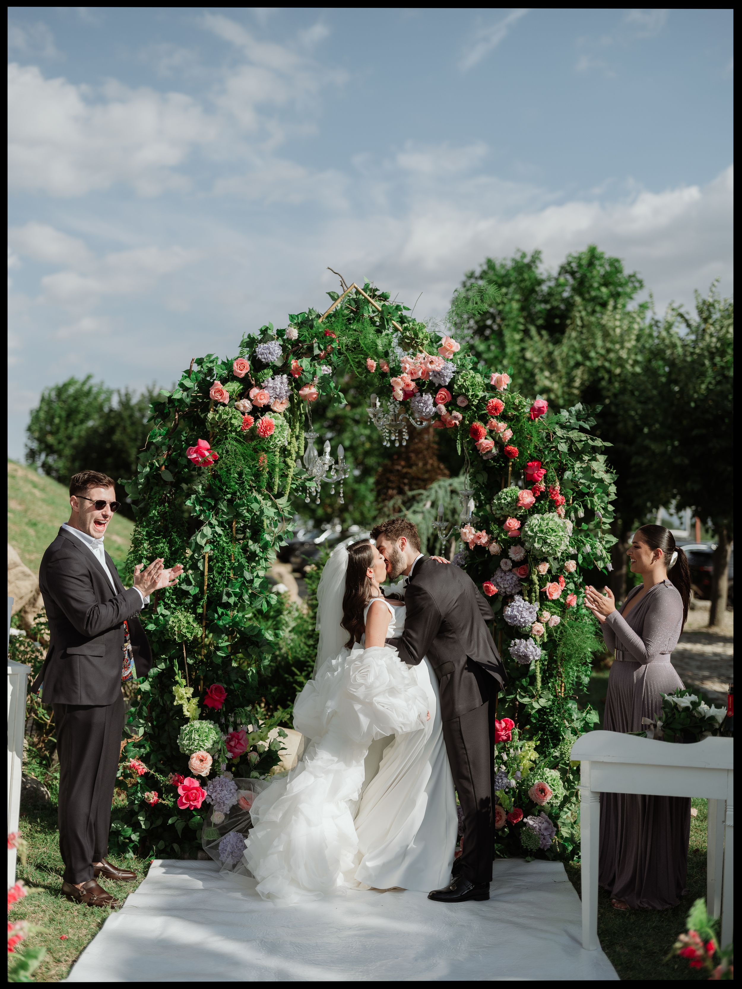 Wedding couple kissing under flower arch after exchanging vows – A newlywed couple shares a kiss beneath a floral arch at their wedding cere