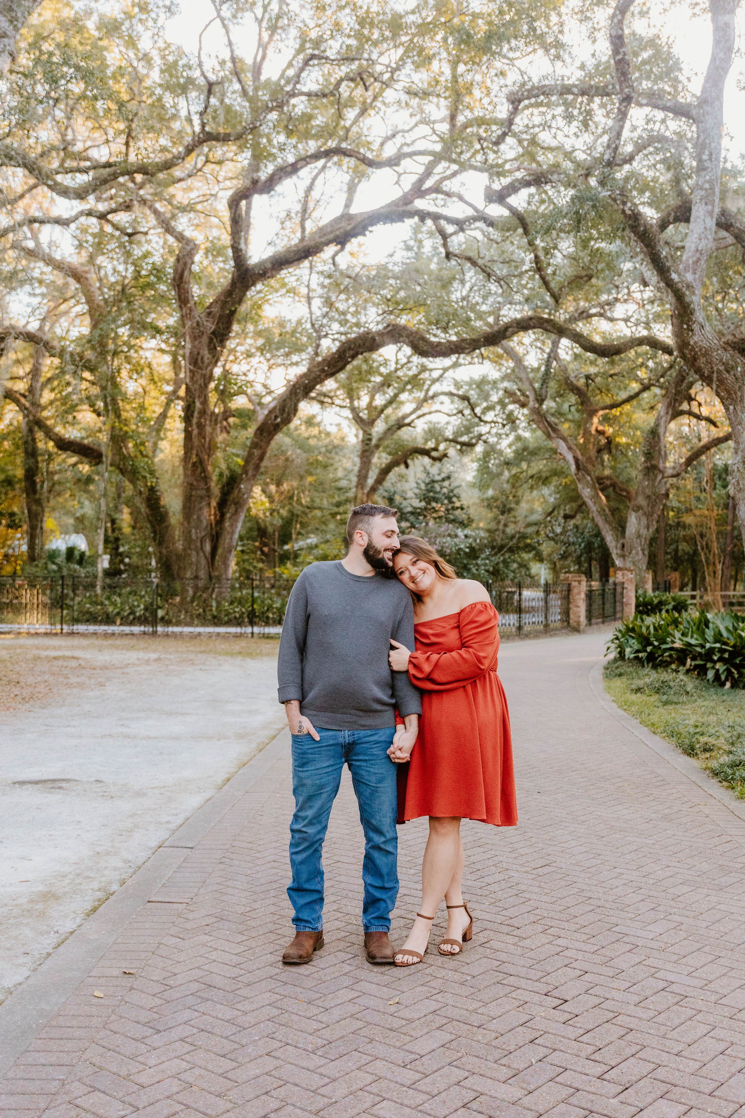 Romantic couple walking along brick pathway under oak trees at sunset.