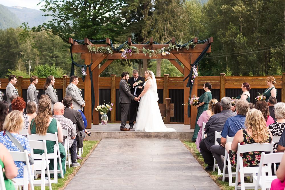 An outdoor ceremony with the bride and groom standing under an arch surrounded by family and friends.