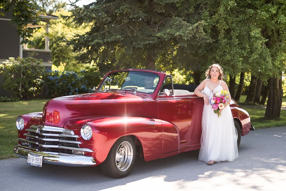A bride standing outside with a red vintage 1947 Chevrolet car with a Corvette engine. Photo taken in Ladner, BC.