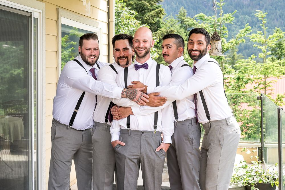 Four groomsmen hug the groom and laugh as they get ready together before the ceremony.