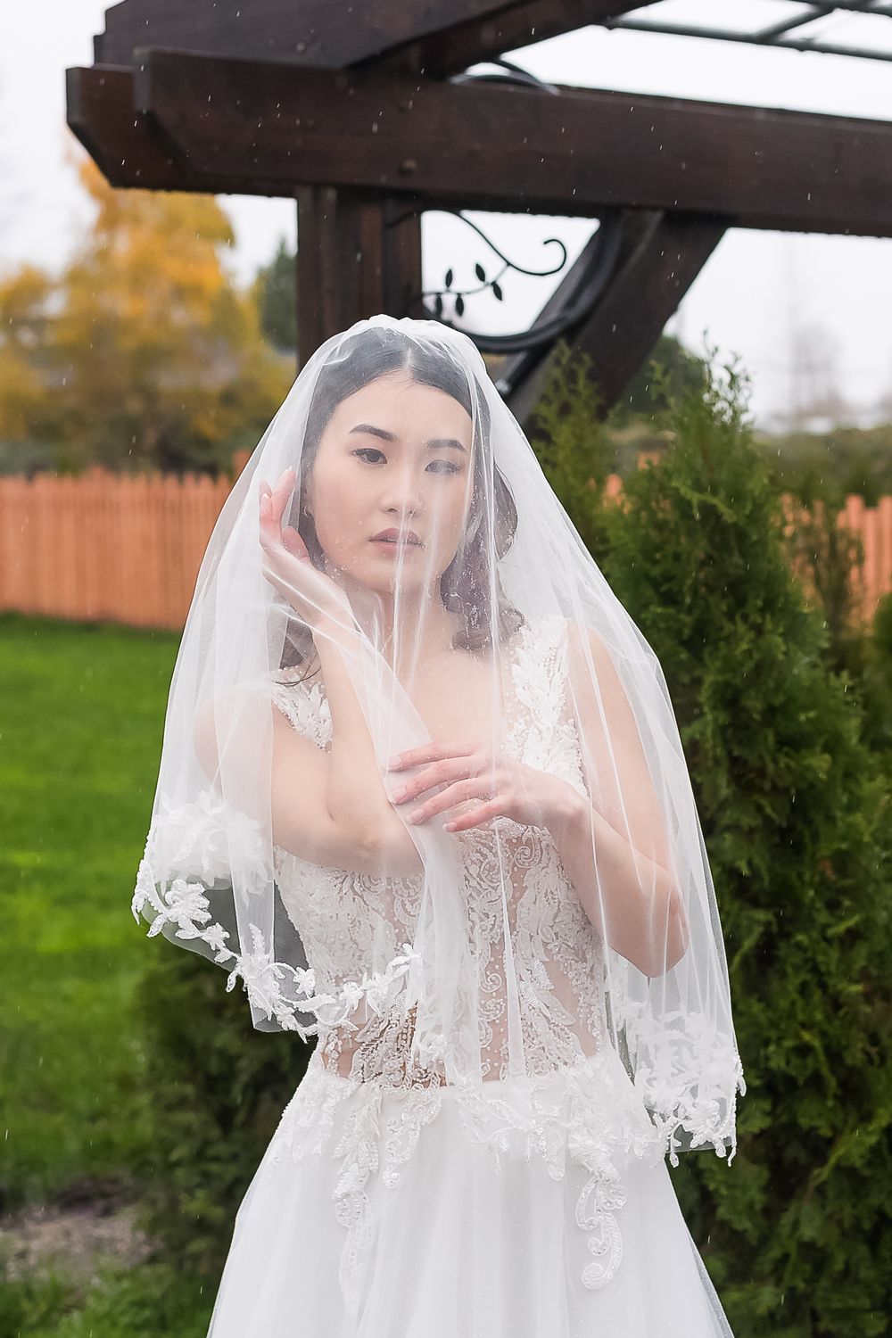 On a rainy fall day, a bride pulls her veil over her head for a dramatic pose.