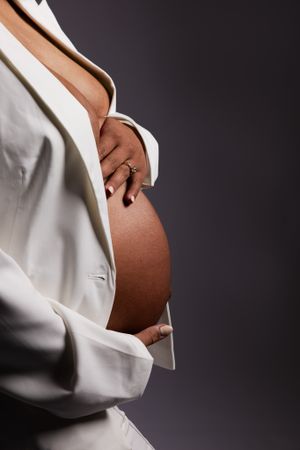 Close-up of expecting mother's belly in white open blazer against dark background.
