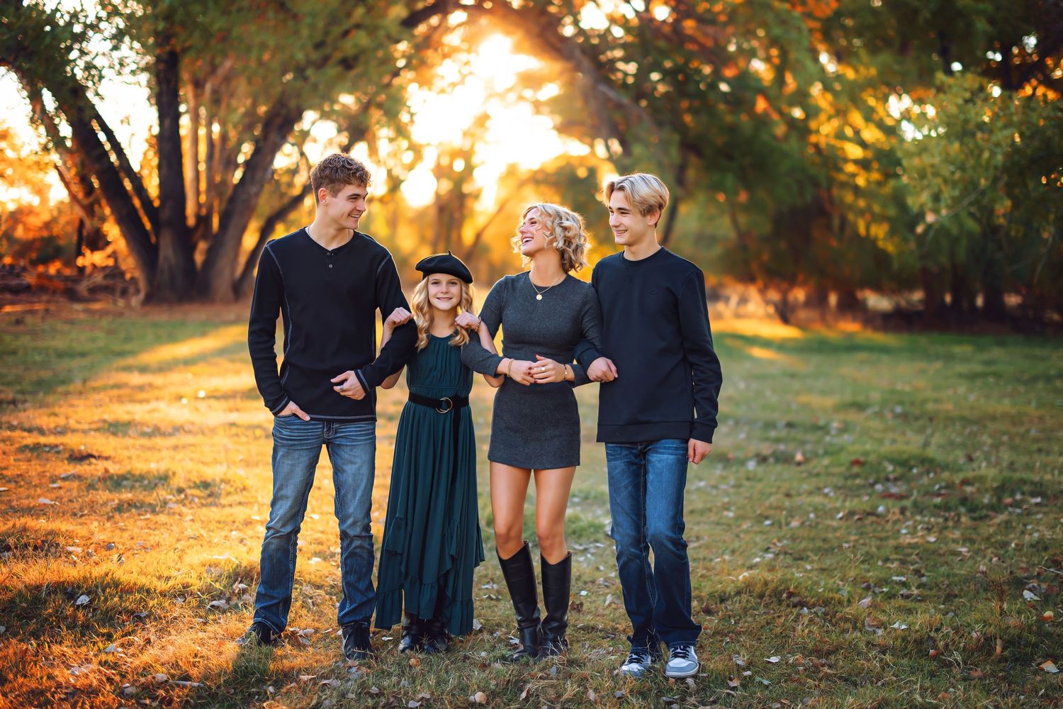 A family poses together outdoors during golden hour with autumn trees in the background.