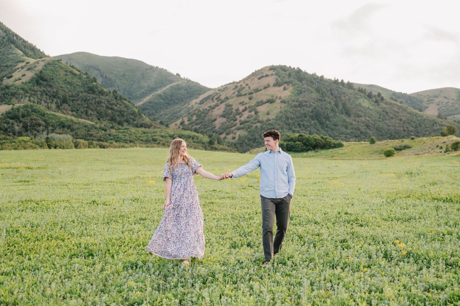 Couple holds hands while walking through a picturesque mountain valley during a photo session.