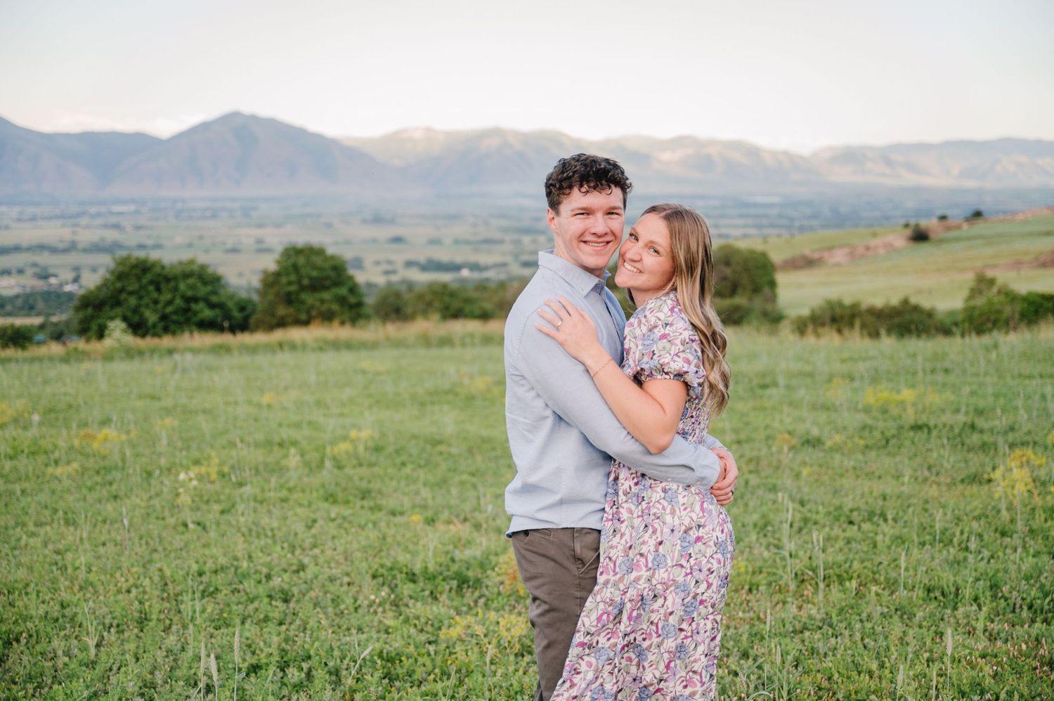 Couple sharing tender moment in mountain meadow with dramatic landscape behind them.
