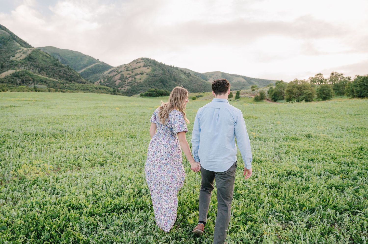 Couple walking hand in hand through mountain meadow with scenic landscape views.