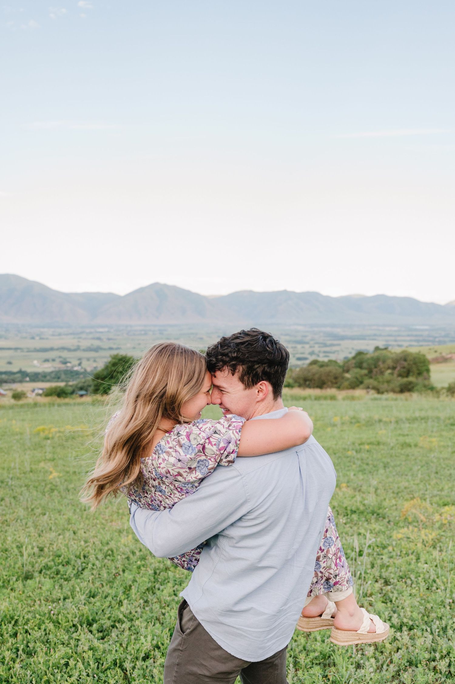 Couple embracing in mountain meadow during sunset with rolling hills in background.