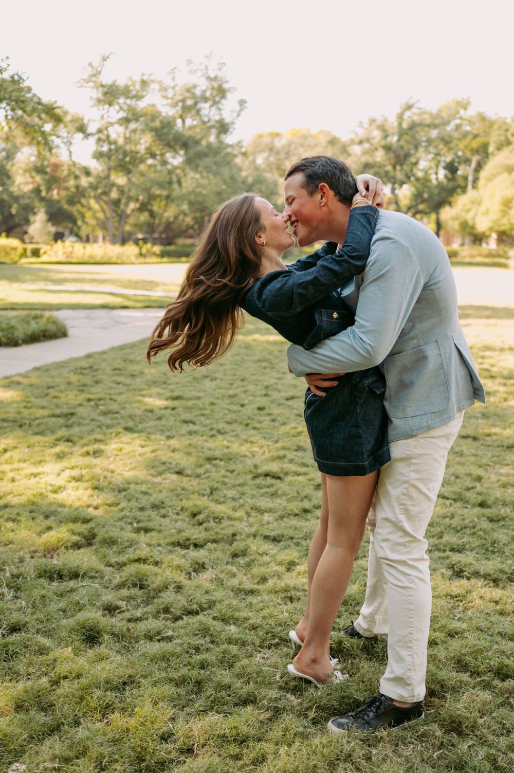 Couple sharing a romantic embrace in a sunlit park after getting engaged.