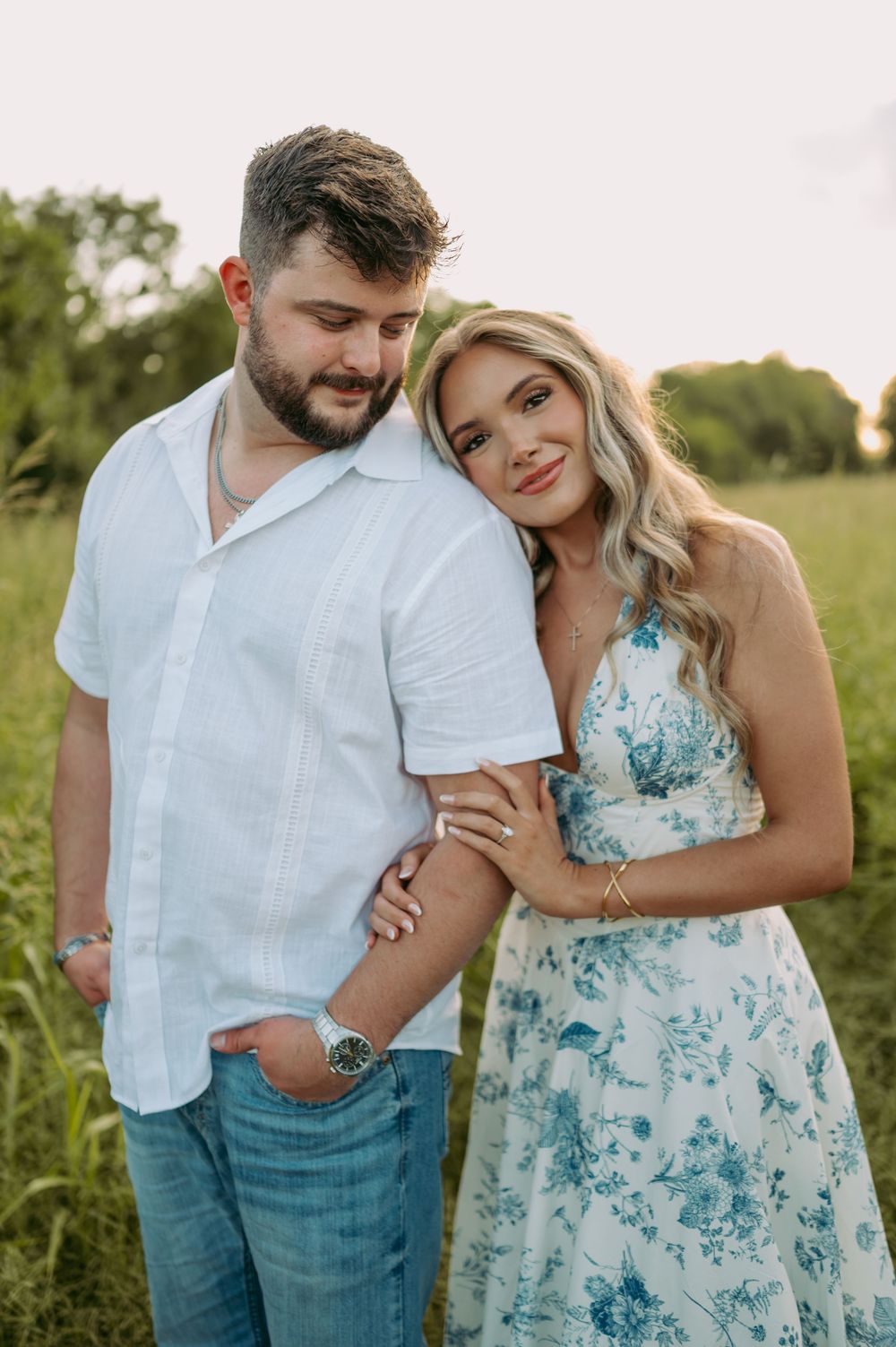 Romantic couple in coordinated blue and white outfits embrace in a sunlit meadow during a summer photoshoot.