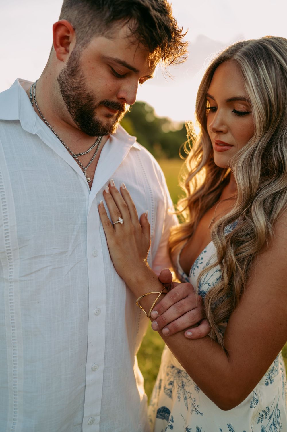 Intimate couple poses in white and blue attire against golden sunset light in a grassy field.