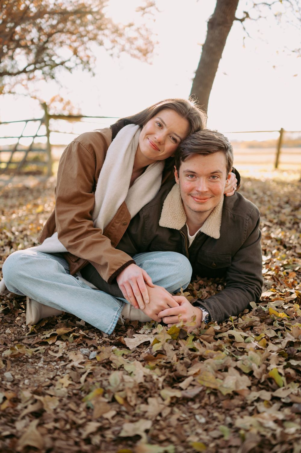 A couple lies together on autumn leaves during a romantic outdoor photo session at sunset.