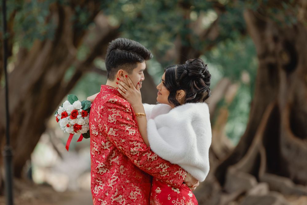 A romantic wedding portrait of a couple in red traditional Chinese dress against a tree-lined backdrop.