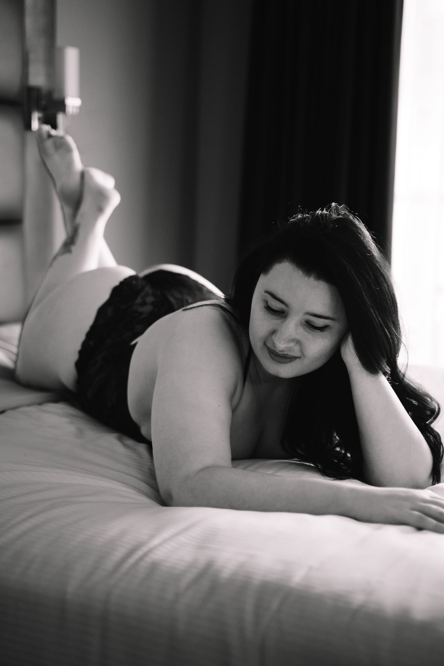 Intimate black and white boudoir photography session showing a woman in dark lingerie posing on a bed.