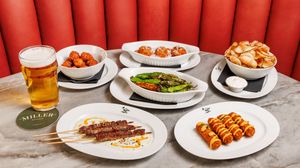 A long row of various restaurant dishes including chips, appetizers and drinks on a marble table.