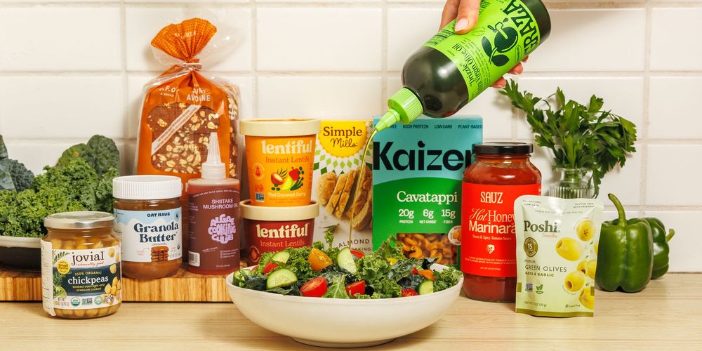 A collection of colorful food jars, sauces, and fresh vegetables arranged in a row against a white background.