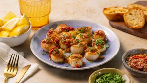 Golden seared scallops with chili glaze on a blue plate, served with garlic bread and lemon wedges.
