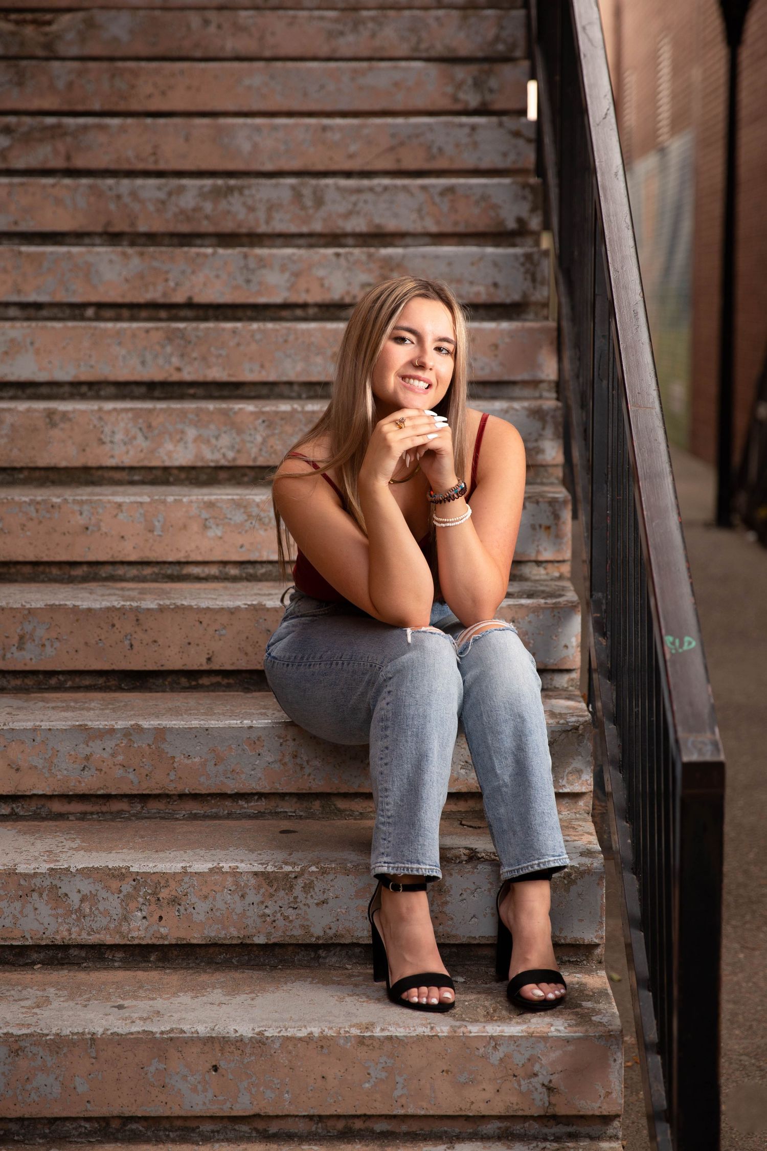 A senior girl in jeans sits casually on rustic wooden stairs in an artistic portrait series.