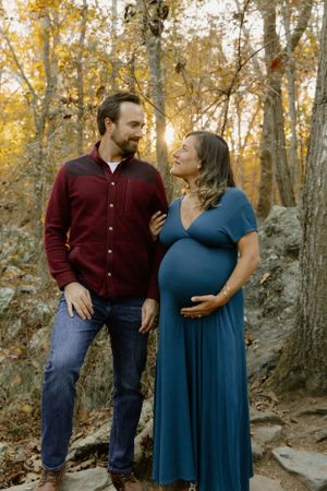 A couple shares an intimate moment in an autumn forest setting, with warm golden light filtering through the trees.