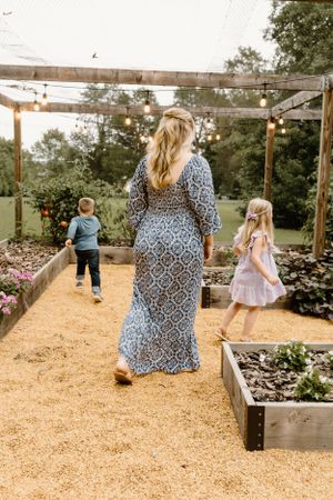 Family explores raised garden beds under pergola with string lights.